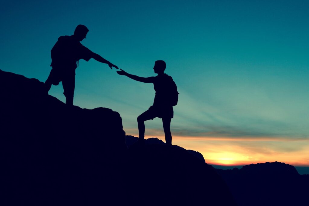 Two hikers on a mountainside at dusk reaching out to help each other